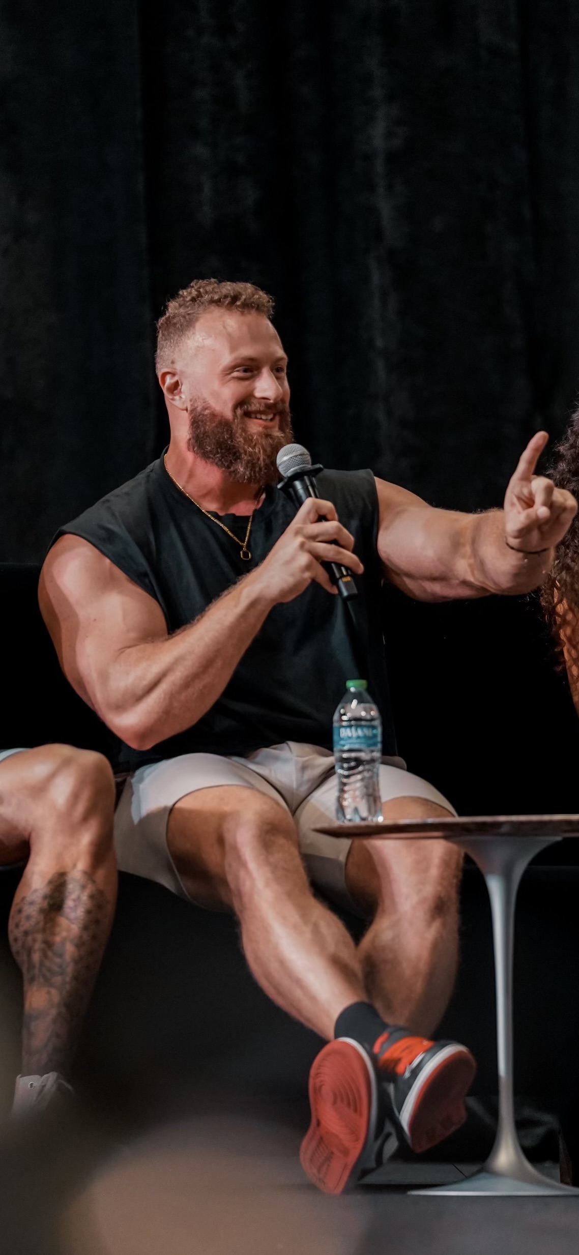 Justin Mihaly speaking on stage at a fitness industry event, holding a microphone